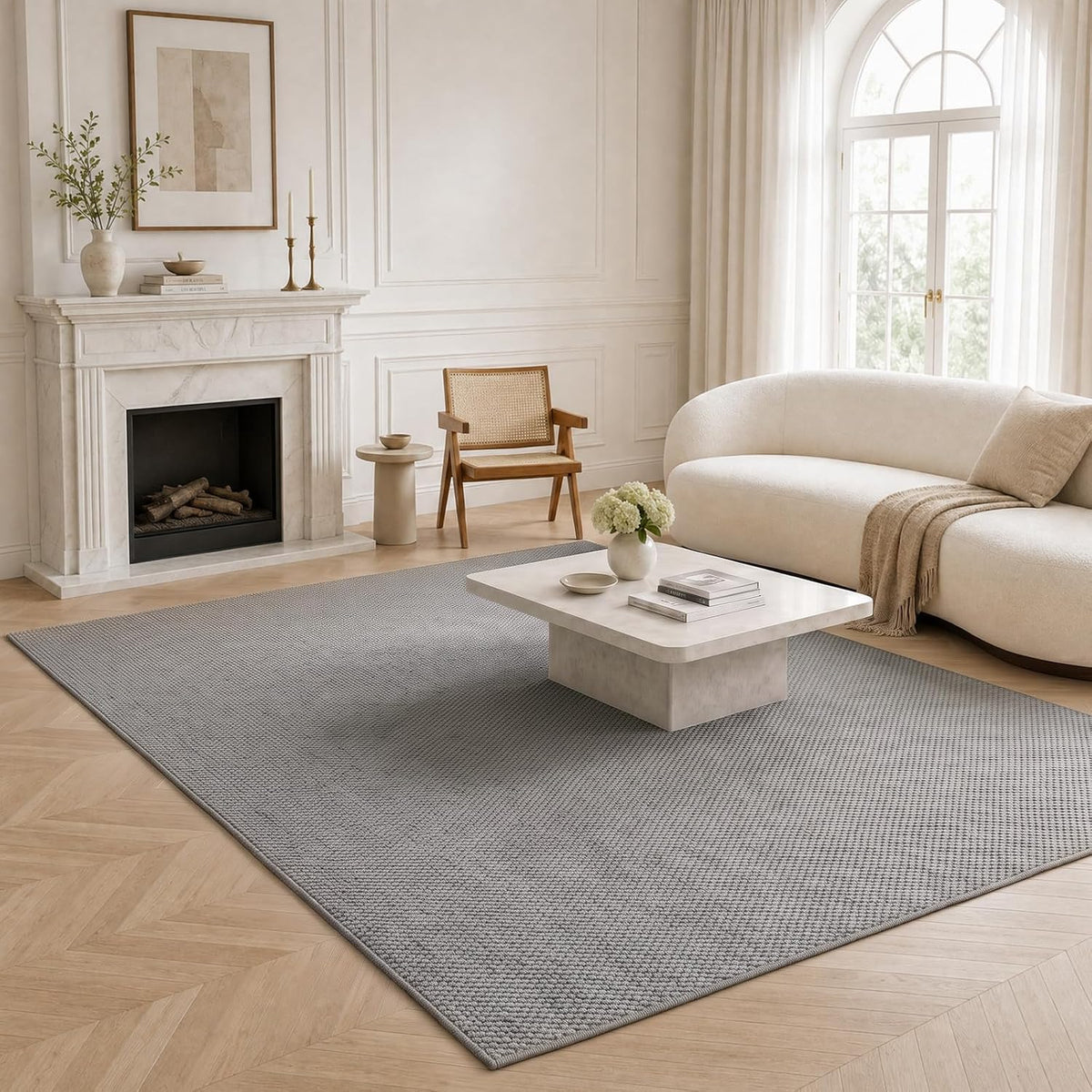 Grey jute-style rug centered in a styled living room under a low coffee table with sofa and fireplace