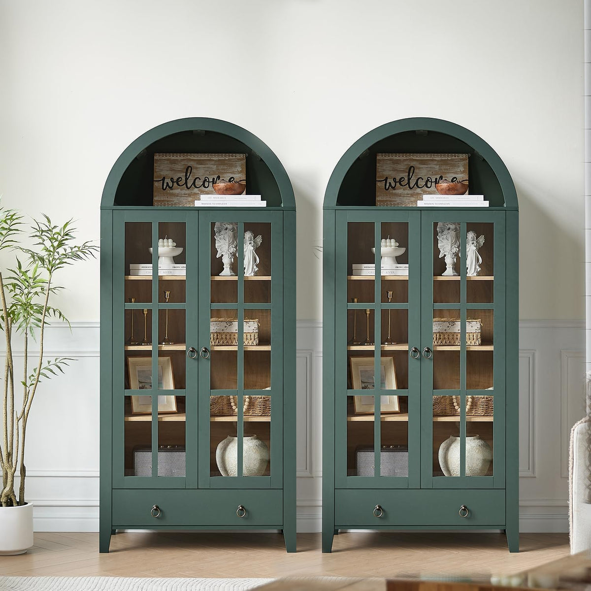 Pair of arched-top green cabinets side-by-side with glass-paned doors and decorative items inside