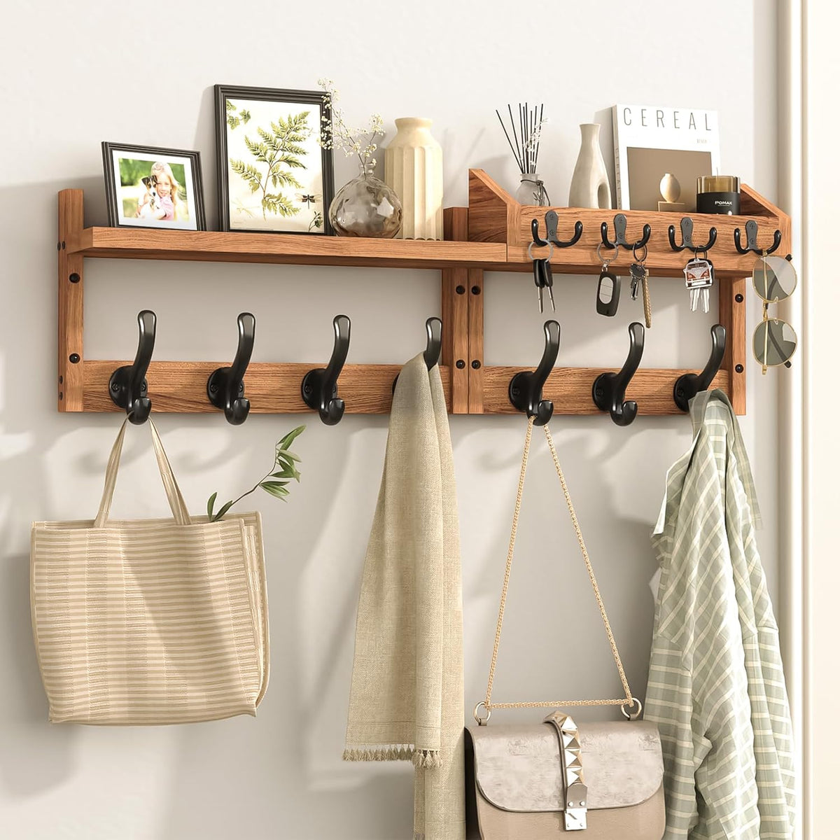 Wall-mounted wooden coat rack with shelf and eleven black hooks holding bags, keys and coats