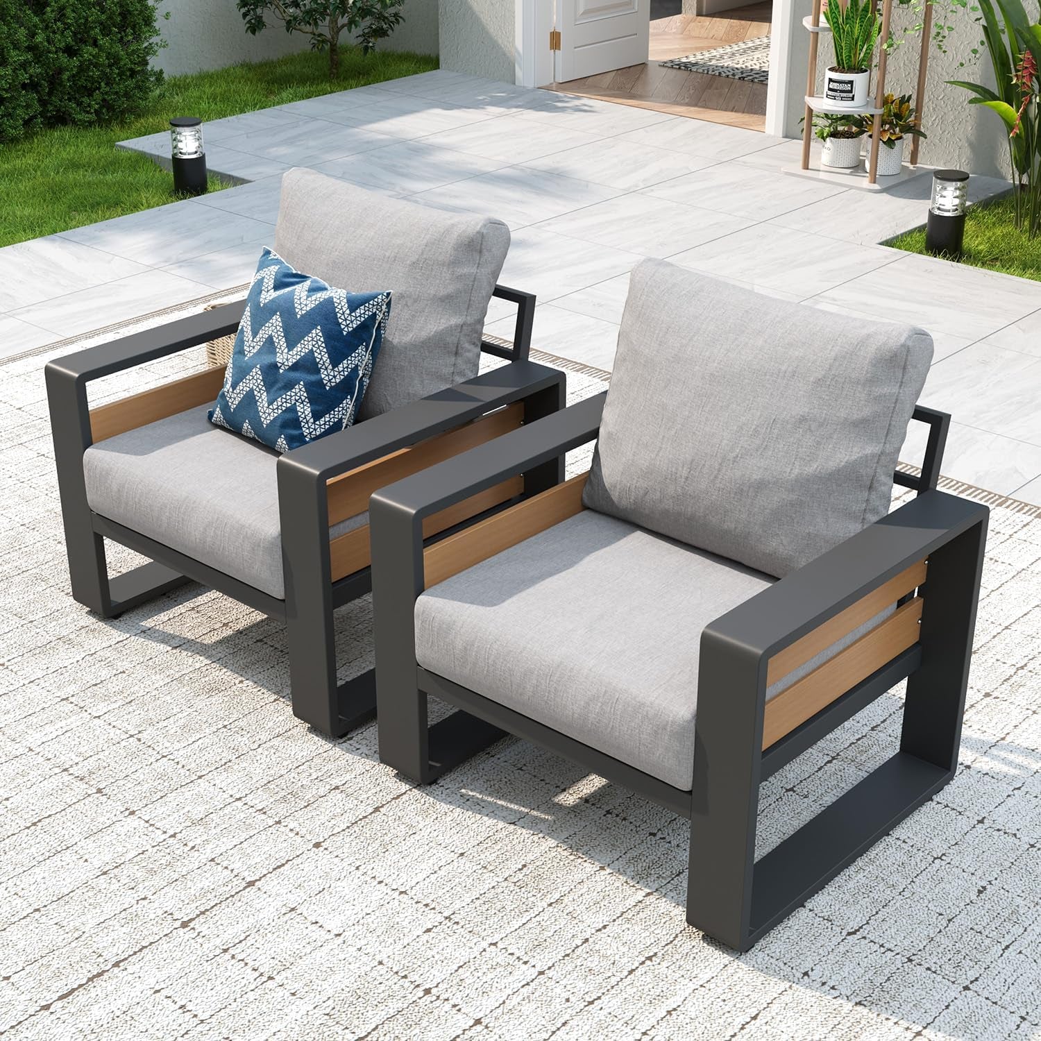Two gray-cushioned outdoor armchairs with dark metal frames and wood-look slats on a patio rug.