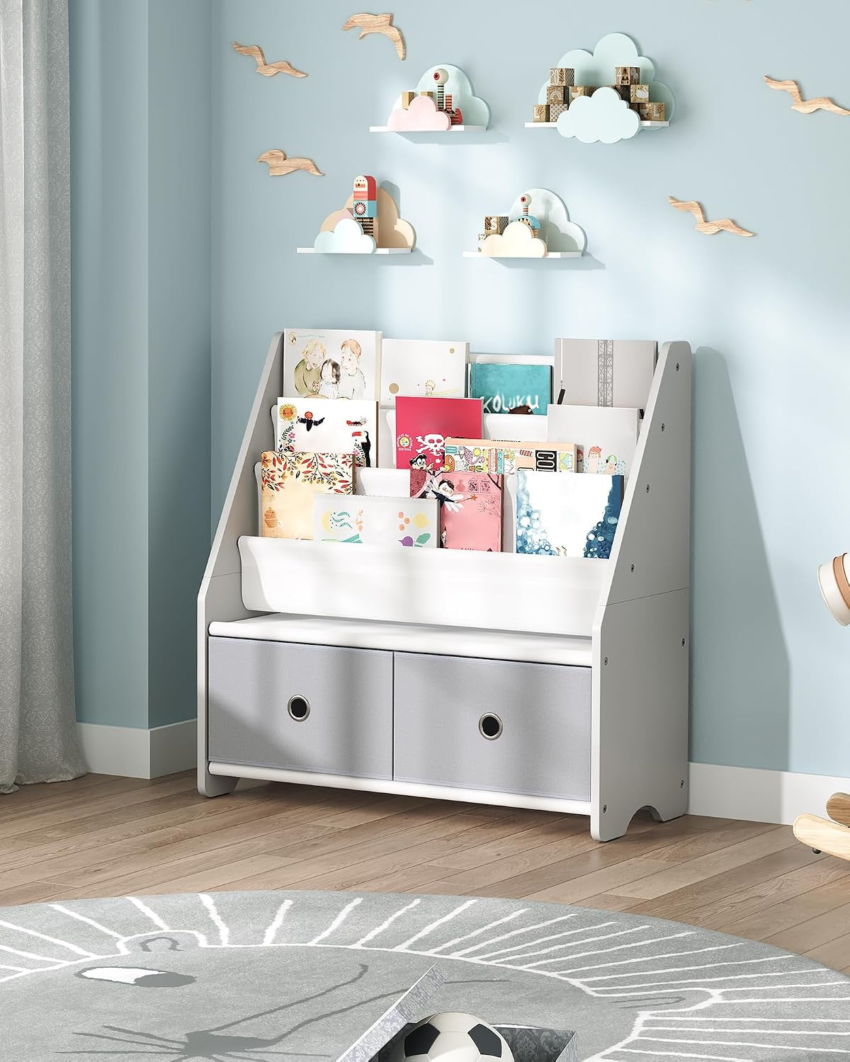 Straight-on view of the white-and-gray children's book rack against a pale blue wall with cloud wall shelves above.