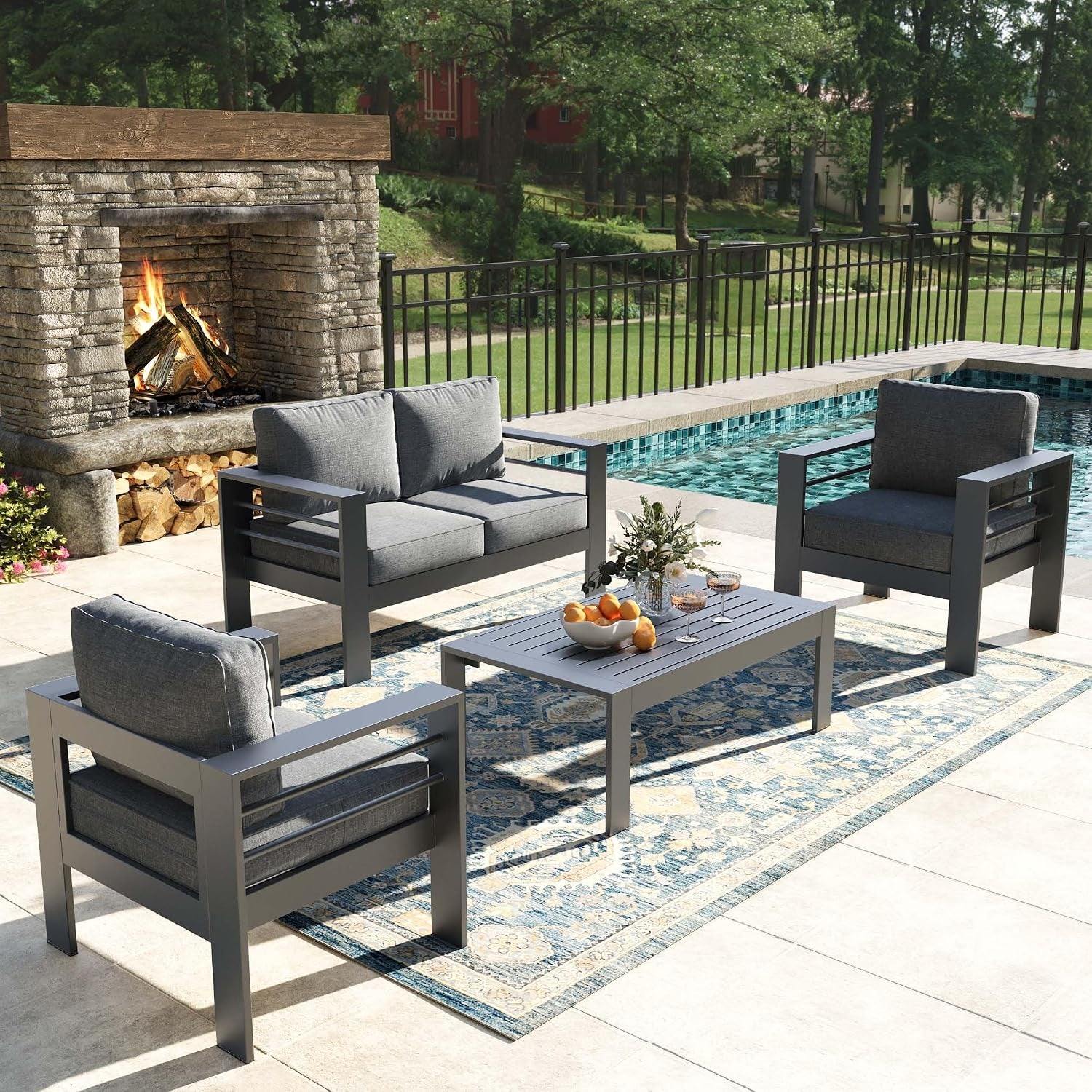 Outdoor seating set in dark gray with slatted coffee table by a pool and fireplace.