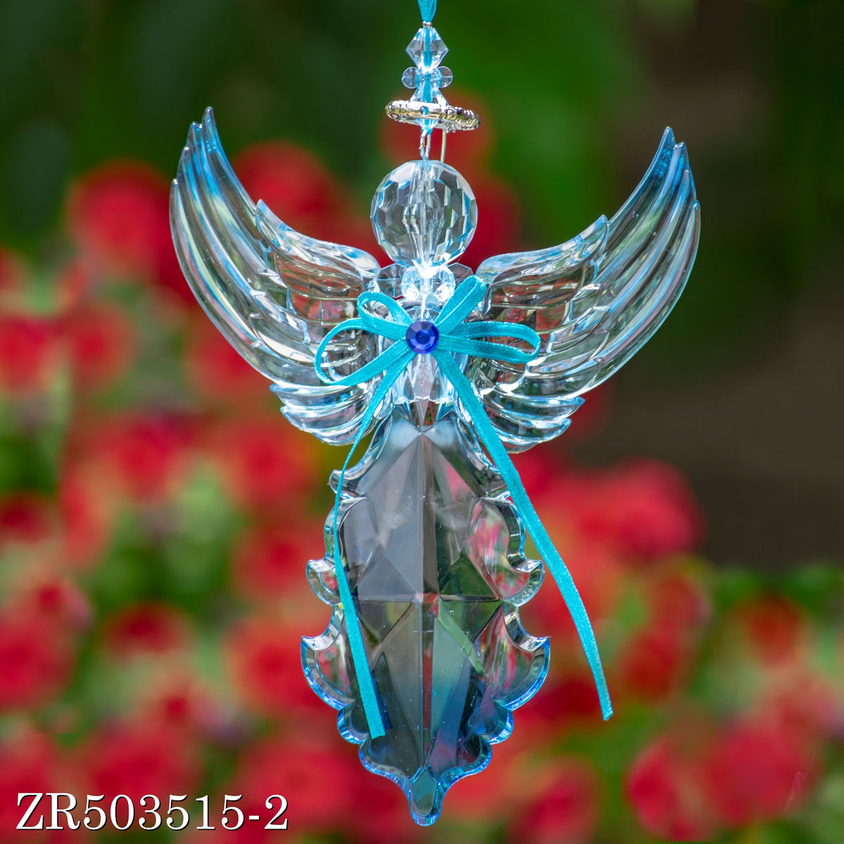 A translucent blue angel hangs against a floral blur, with raised wings and long turquoise ribbon tails.