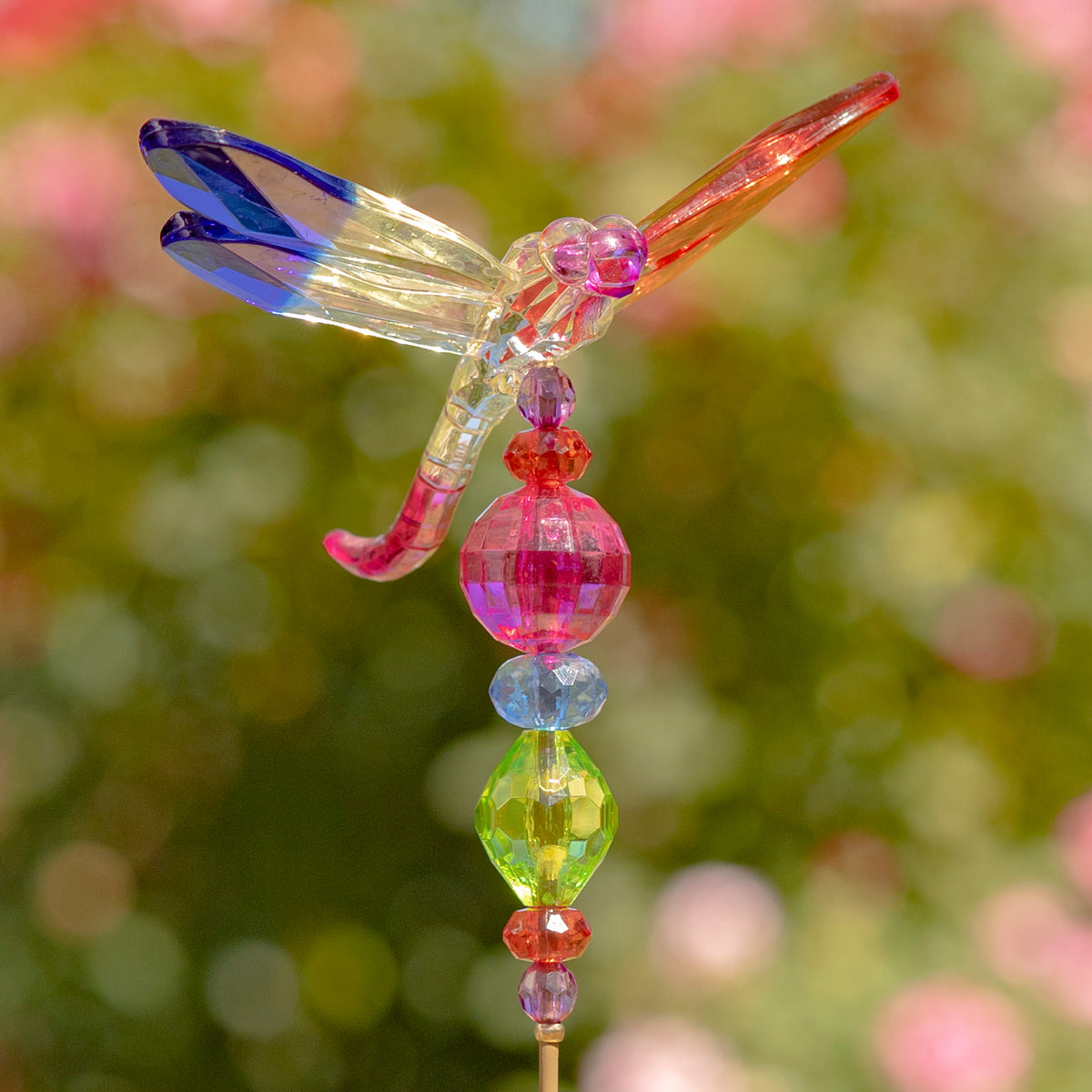Colorful dragonfly with blue, gold, and orange wings atop stacked pink, green, and orange beads.