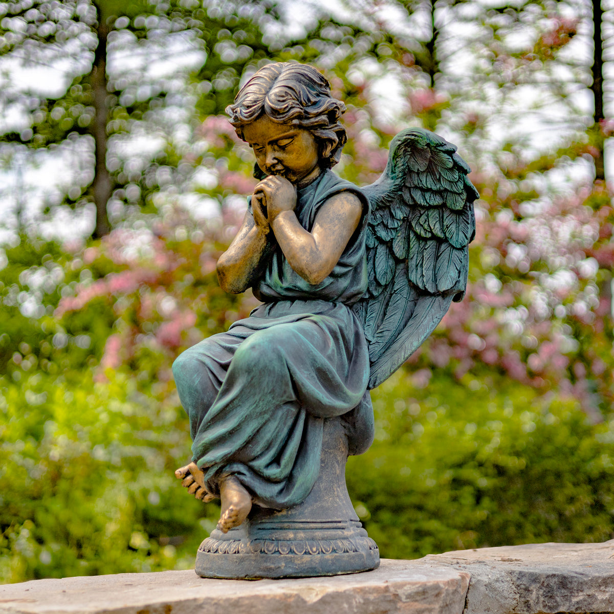 Side view of the seated angel statue on a stone ledge, showing its wing and folded pose.