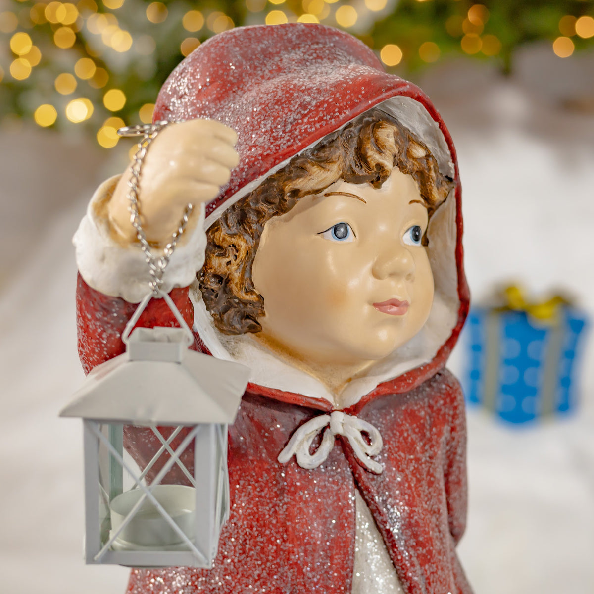 Close-up of a hooded childlike figure in a red cloak holding a hanging lantern.