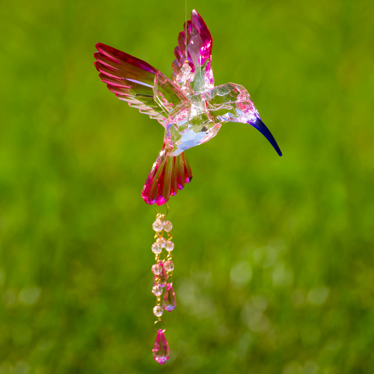 Pink and clear faceted hummingbird ornament with dangling beads against a blurred green background.