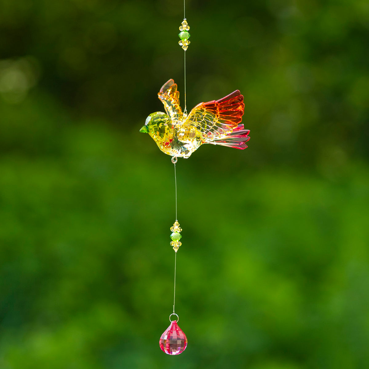A colorful acrylic bird with raised wings hangs on a beaded strand above a pink balloon-shaped drop.
