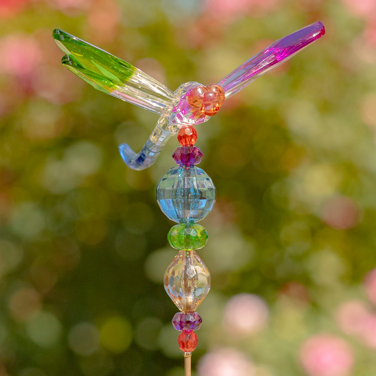 A translucent dragonfly stake with green and purple wings above a strand of blue, green and amber beads.
