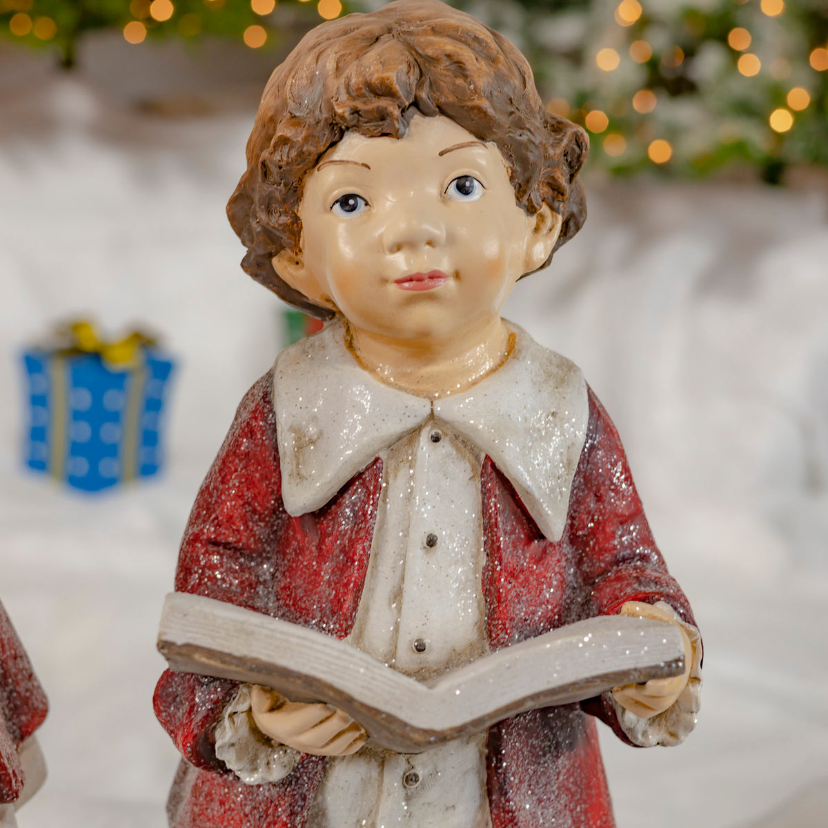 Close view of a curly-haired figure in a red cloak holding an open book.