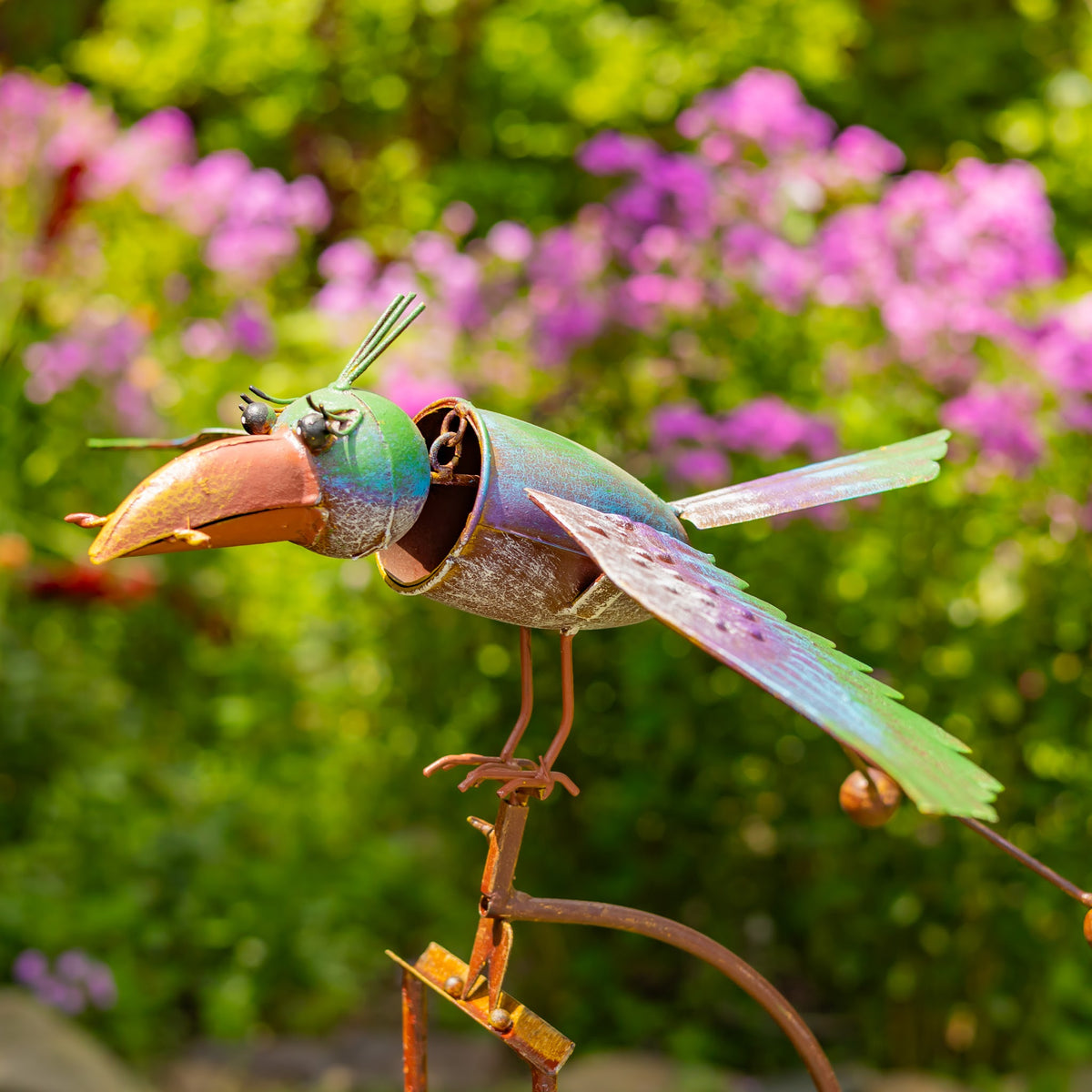 Side view of colorful cockatoo garden stake with wings spread among flowers