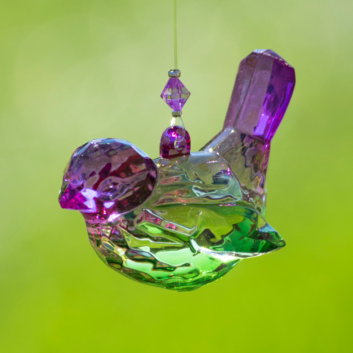 Faceted clear bird ornament with purple accents and green reflections, hanging against a lime-green background.