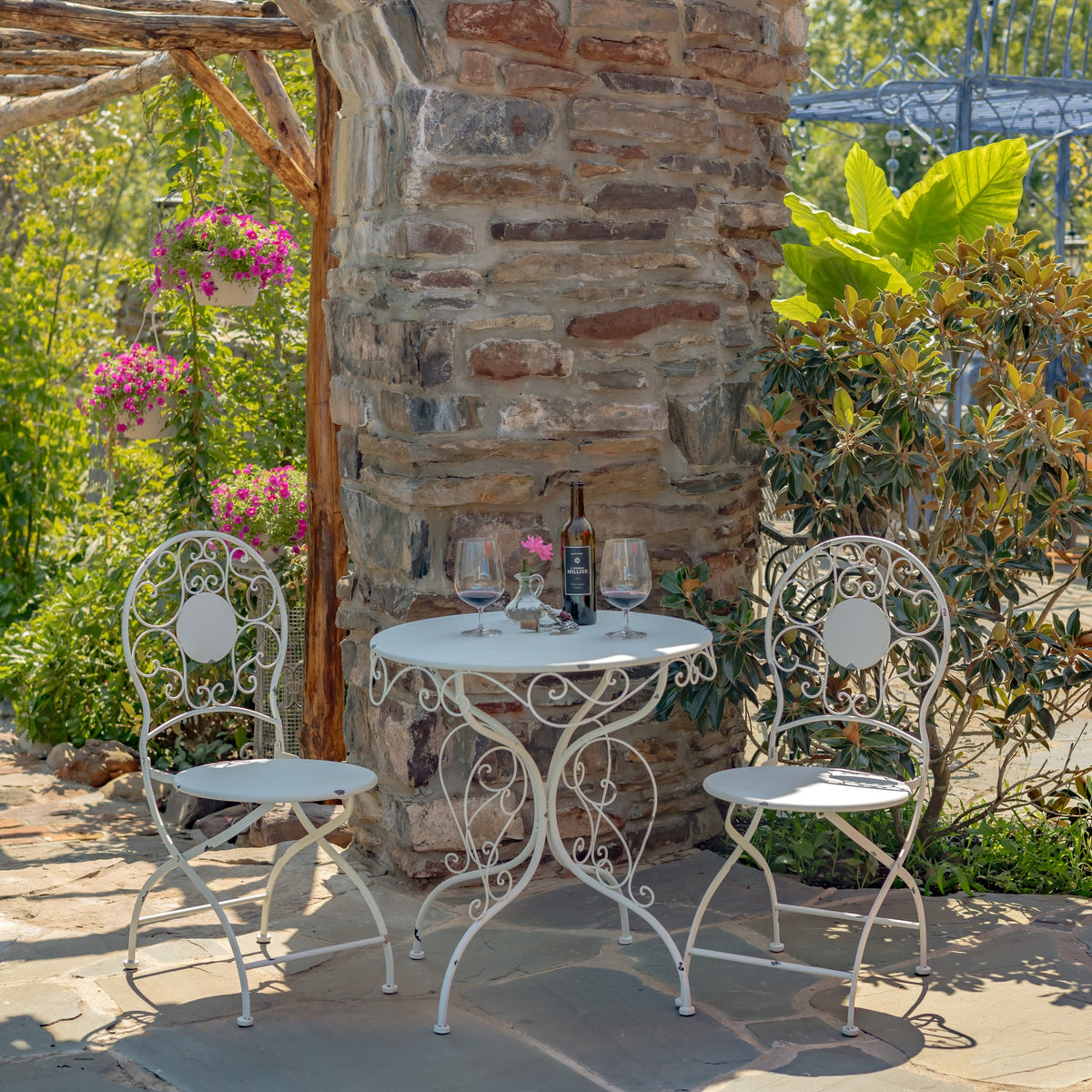 White metal bistro table and two folding chairs arranged in a garden patio