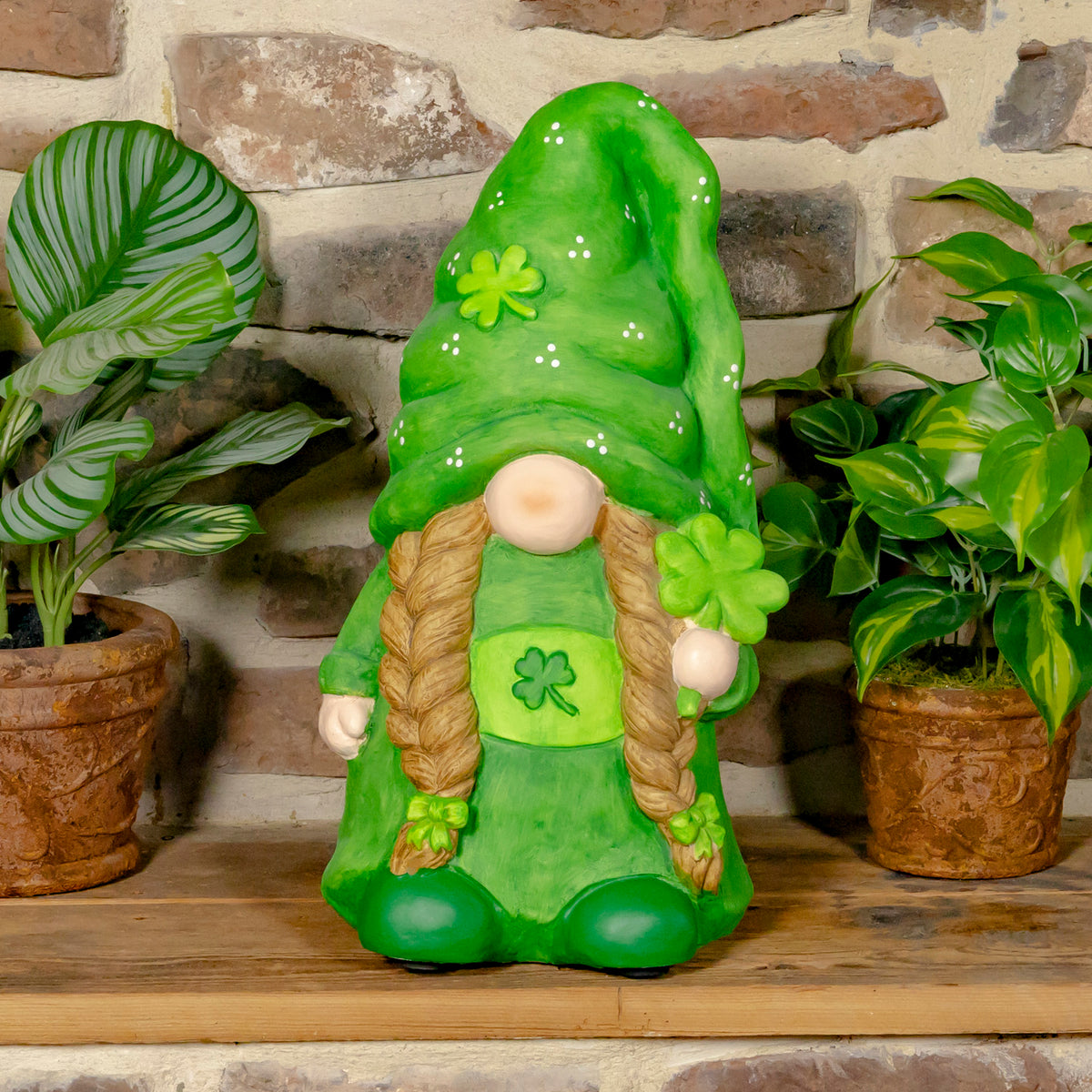 A green garden gnome with long braids holds a three-leaf clover between two potted plants.
