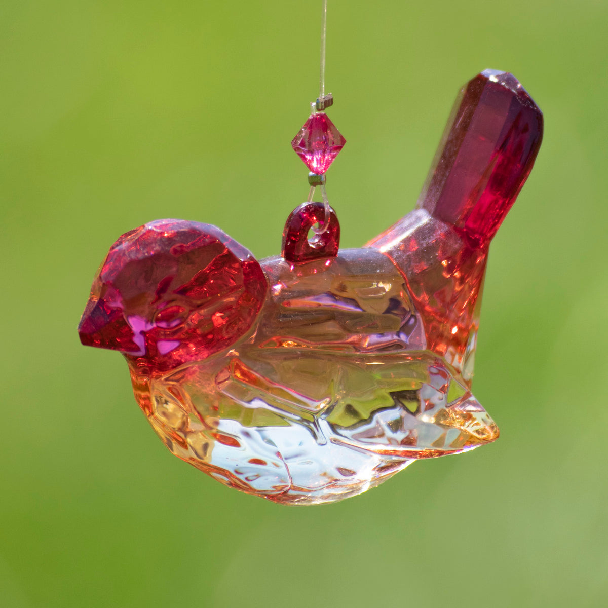 Faceted clear bird ornament with red and amber reflections, suspended against a lime-green background.