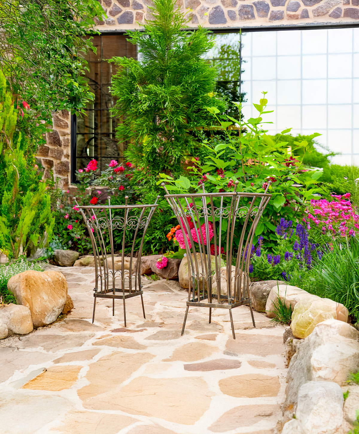 Two round metal trellis stands displayed among flowers on a stone garden path.