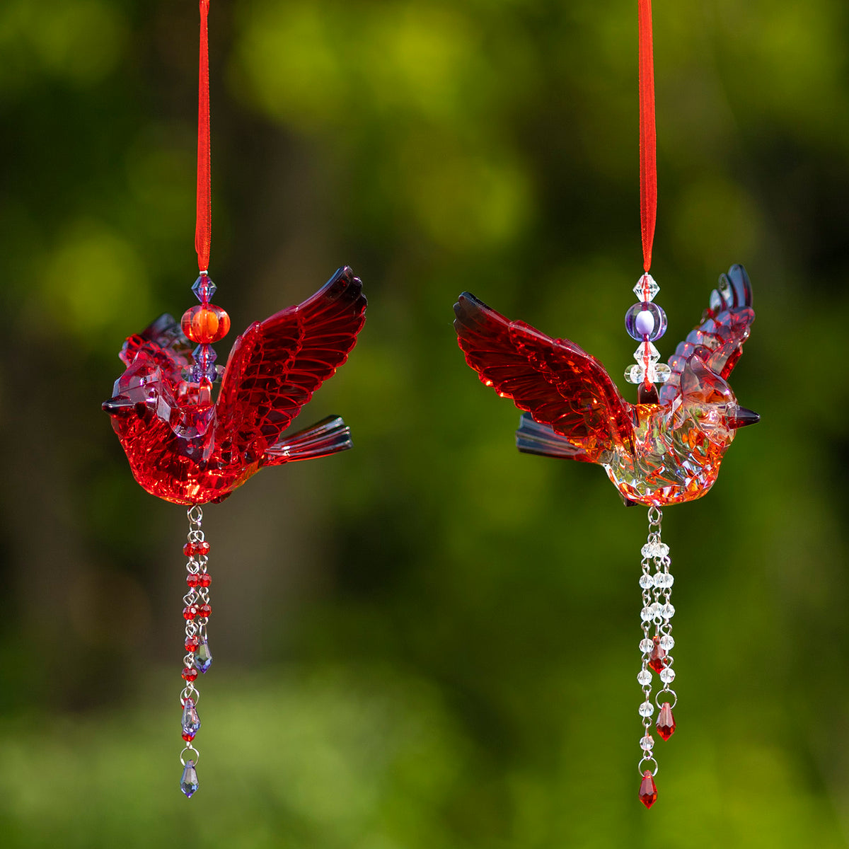 Two faceted bird ornaments hang side by side, one red and one clear with red wings, each with a beaded tassel.