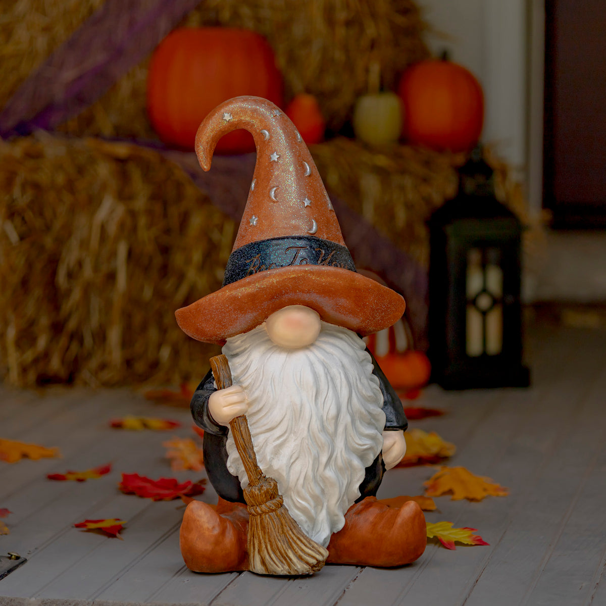 Warlock garden gnome with brown hat and broom in a Halloween display with pumpkins