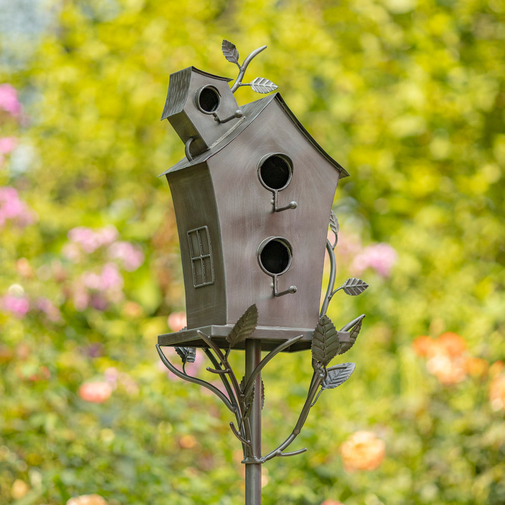 Metal A-frame birdhouse on a stake, angled front view in a colorful garden