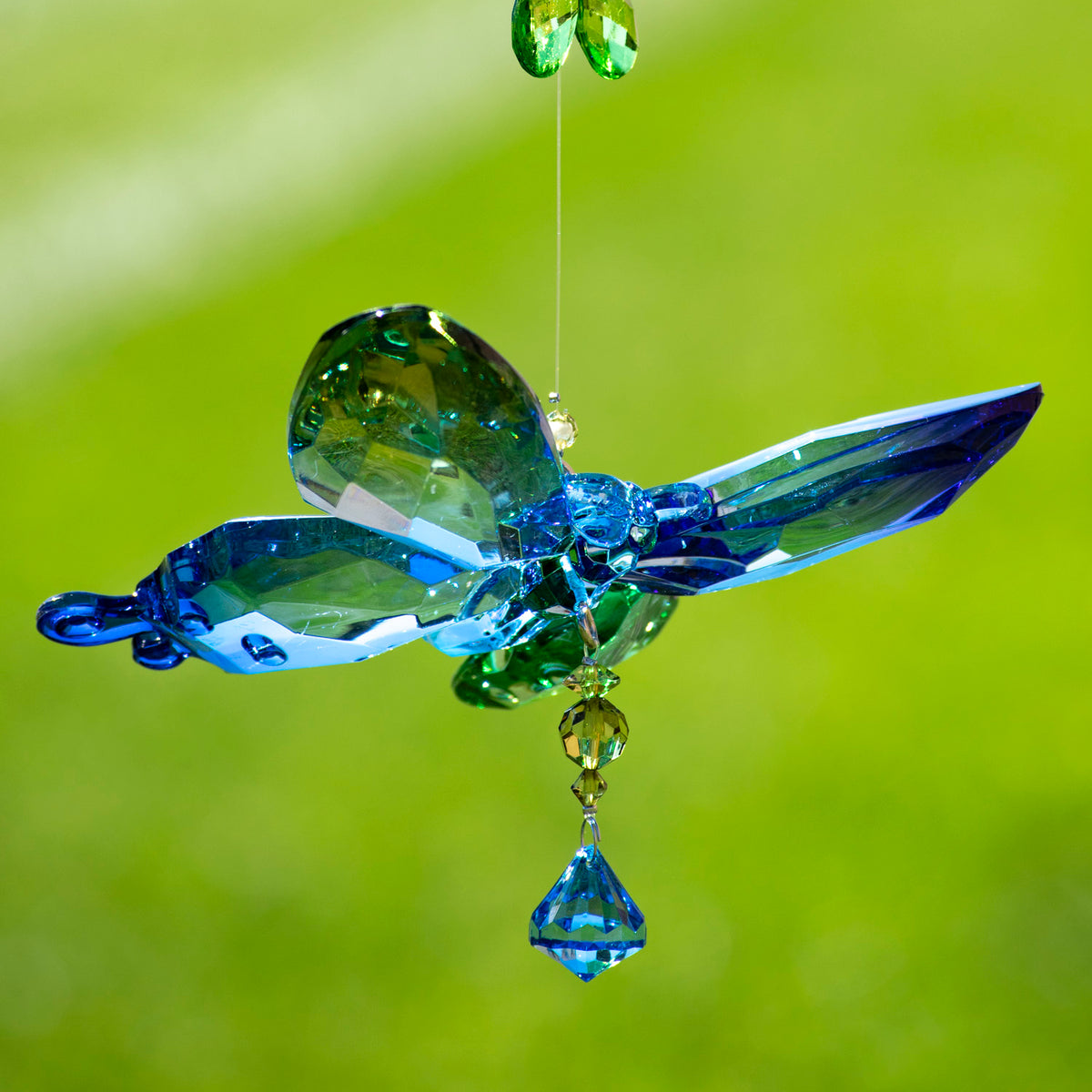 Blue and green faceted butterfly ornament suspended against a green background, with a blue crystal drop.