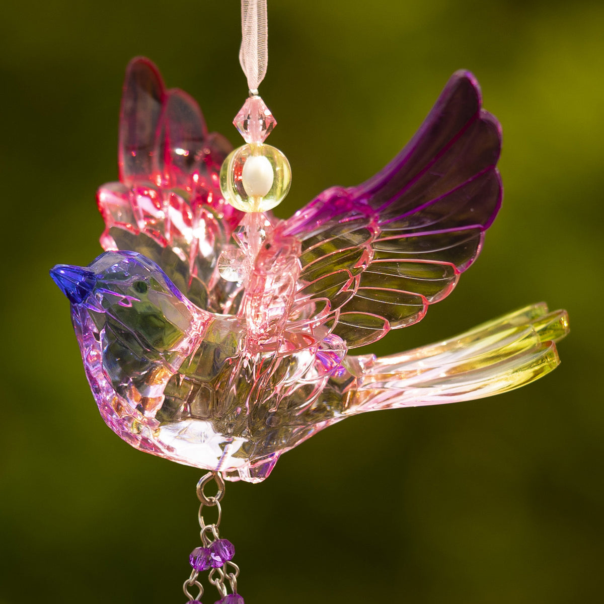 Close-up of a translucent bird ornament showing its layered pink and purple wings, ribbon, and dangling beads.