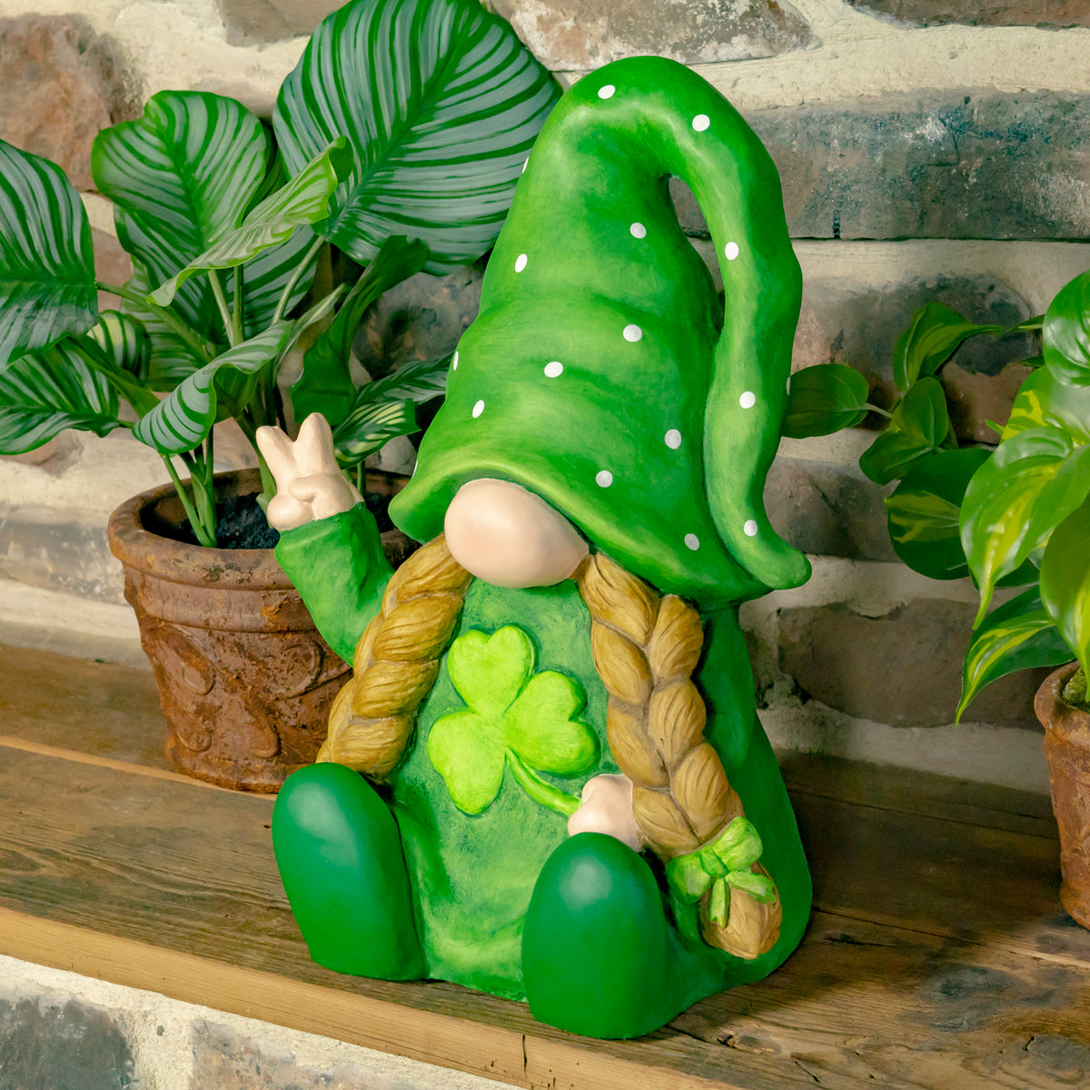 Seated garden gnome in a green spotted hat holds up a peace sign, with a clover on its outfit.