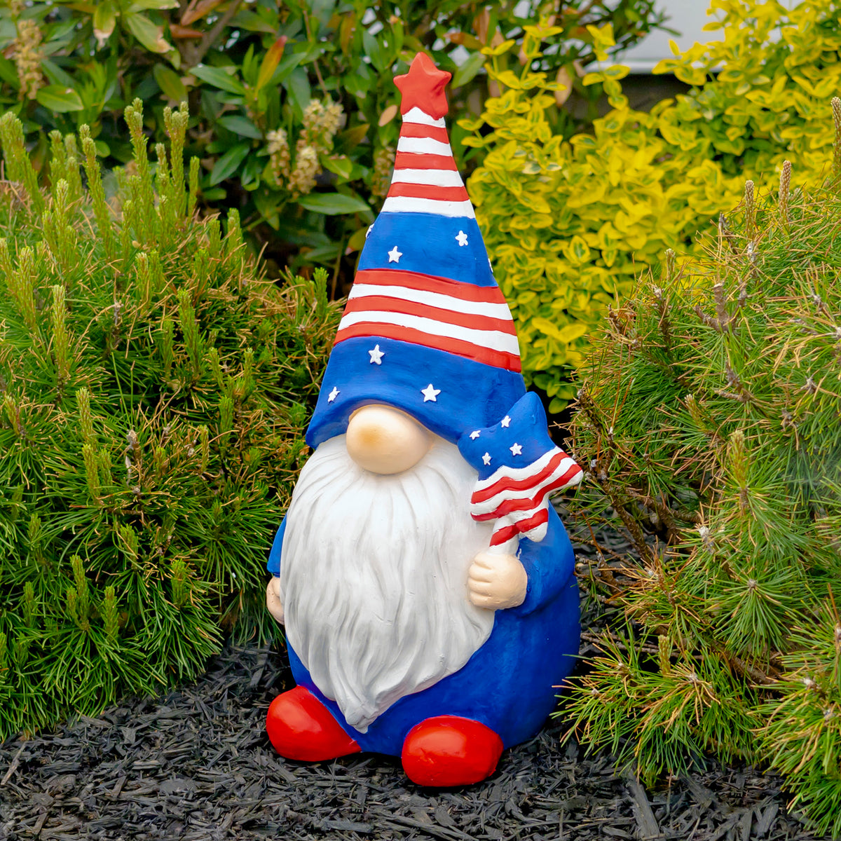 Bearded garden gnome in a star-spangled hat holding a striped star-topped ornament among shrubs.