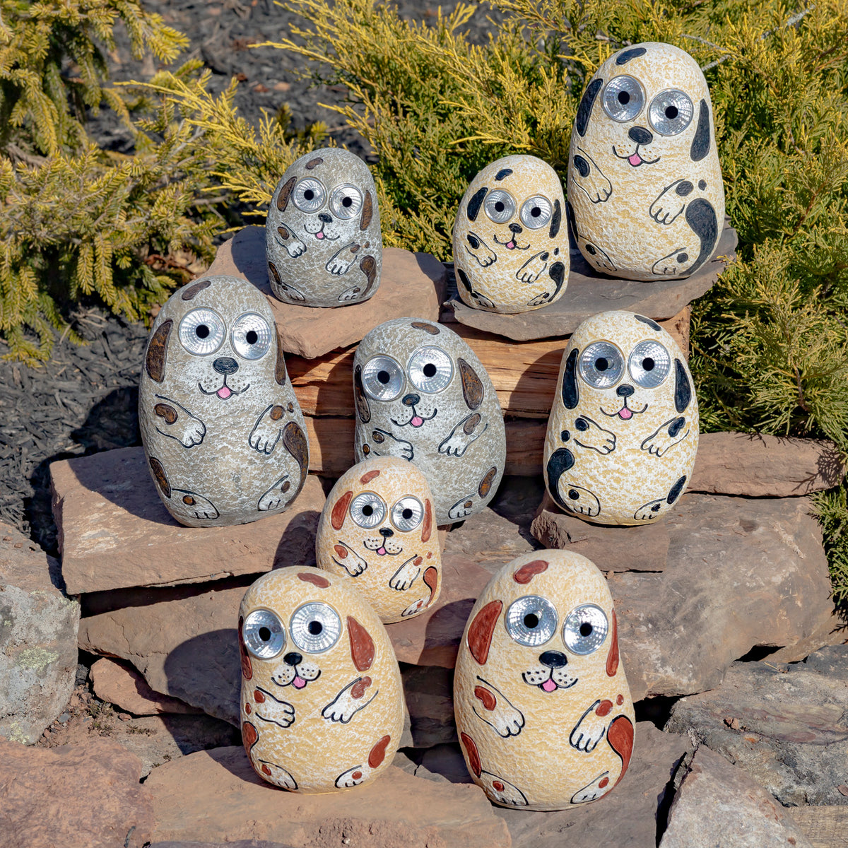 A group of painted stone dogs in ivory, gray, and tan is arranged on rocks outdoors.