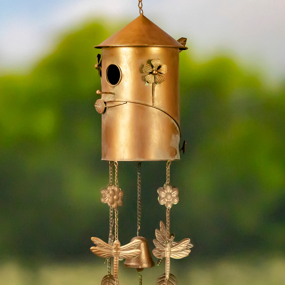 Closer view of the copper-toned birdhouse wind chime, showing its conical roof, flower details, and hanging birds