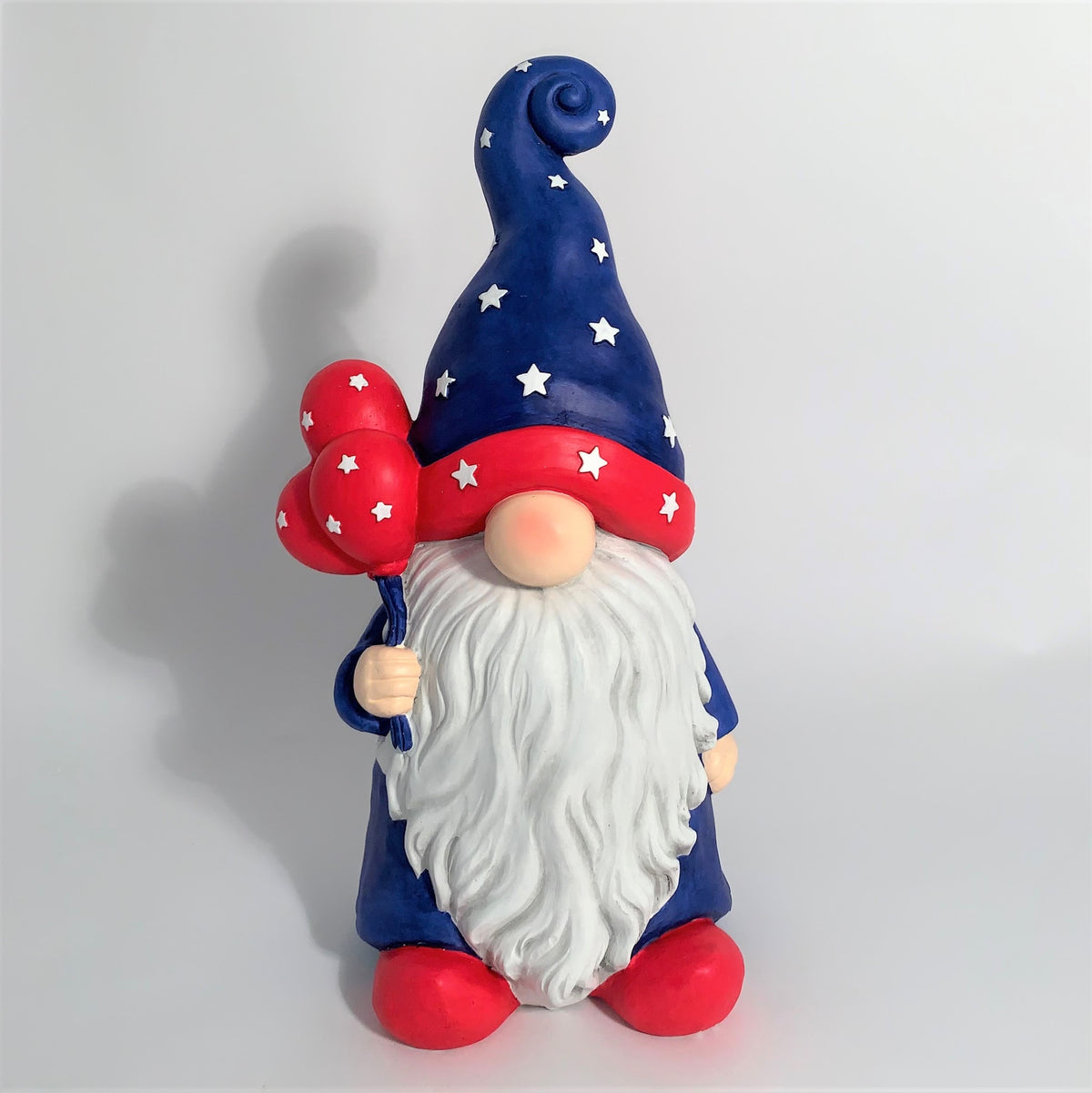 Front view of a red, white and blue garden gnome holding red balloons