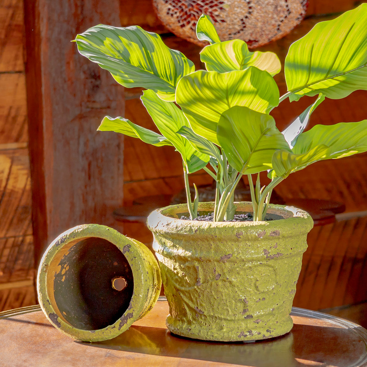 A planted green pot stands beside a matching pot tipped on its side, showing its dark interior.