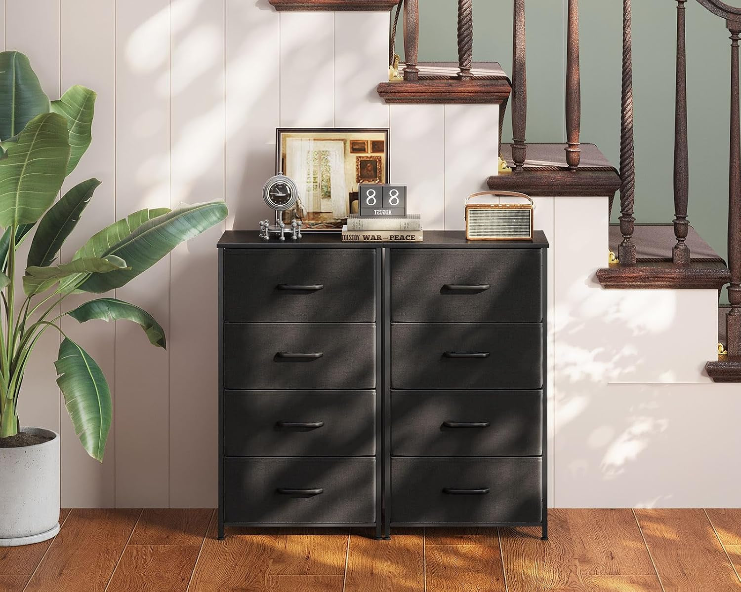 Two narrow four-drawer dressers side by side under a stair, styled with decor on top.