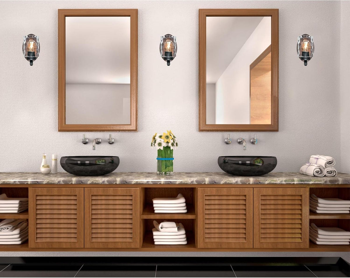 Bathroom vanity scene with two wall sconces flanking mirrors, showing wood-tone back plates and clear hammered glass shades
