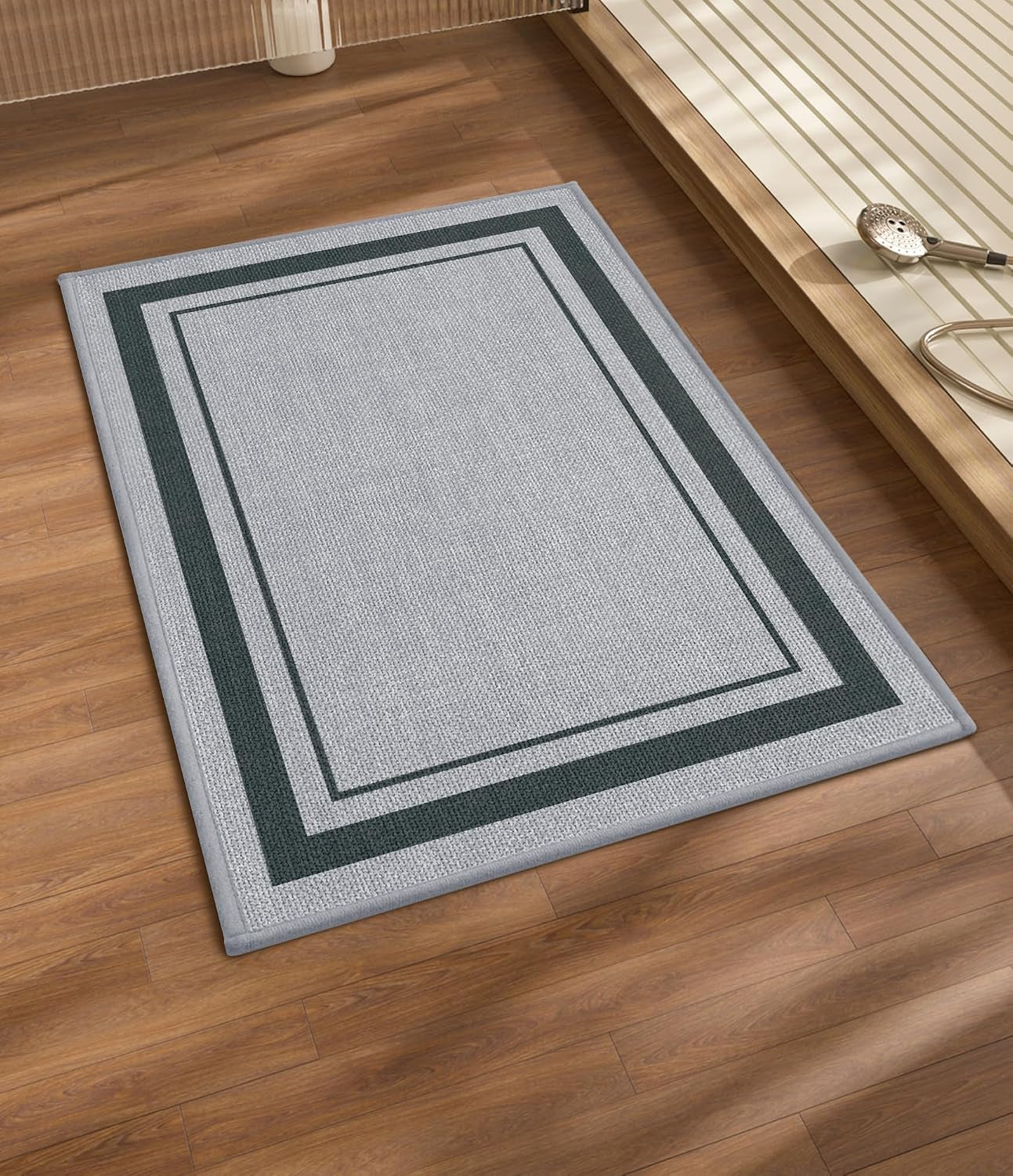 Light gray rectangular mat with dark double border placed on wood flooring next to a shower platform.