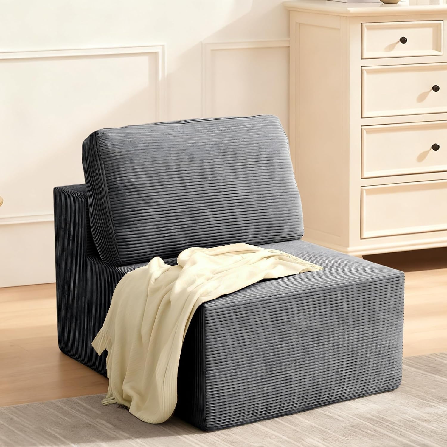 Single gray armless modular chair module with a back cushion and a light cream throw draped over the seat.