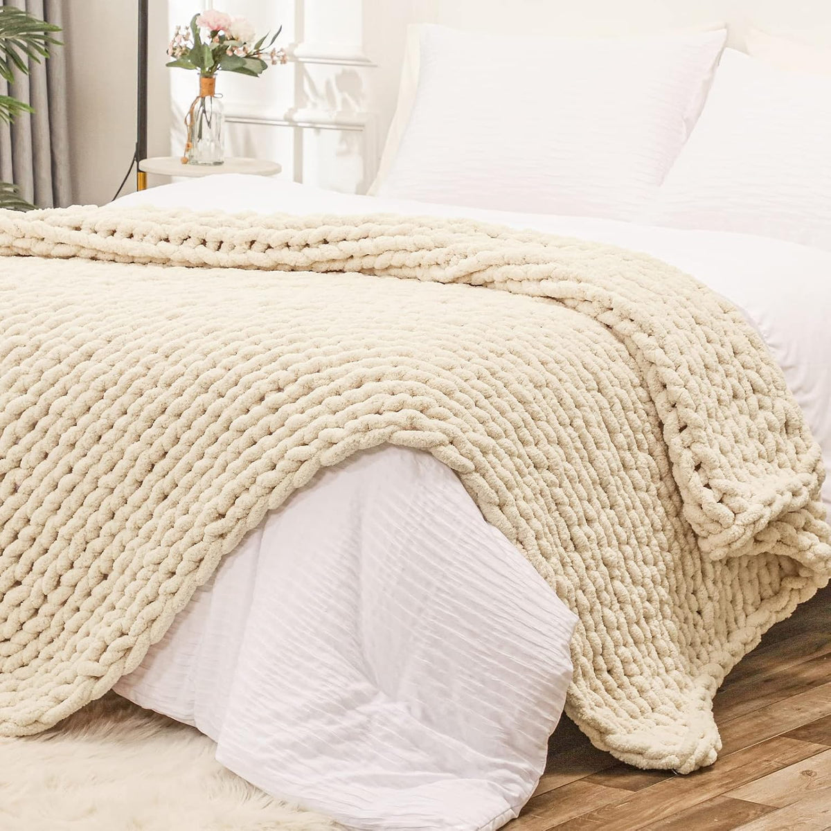 Beige chunky knit throw draped across the foot of a white bed in a bright bedroom