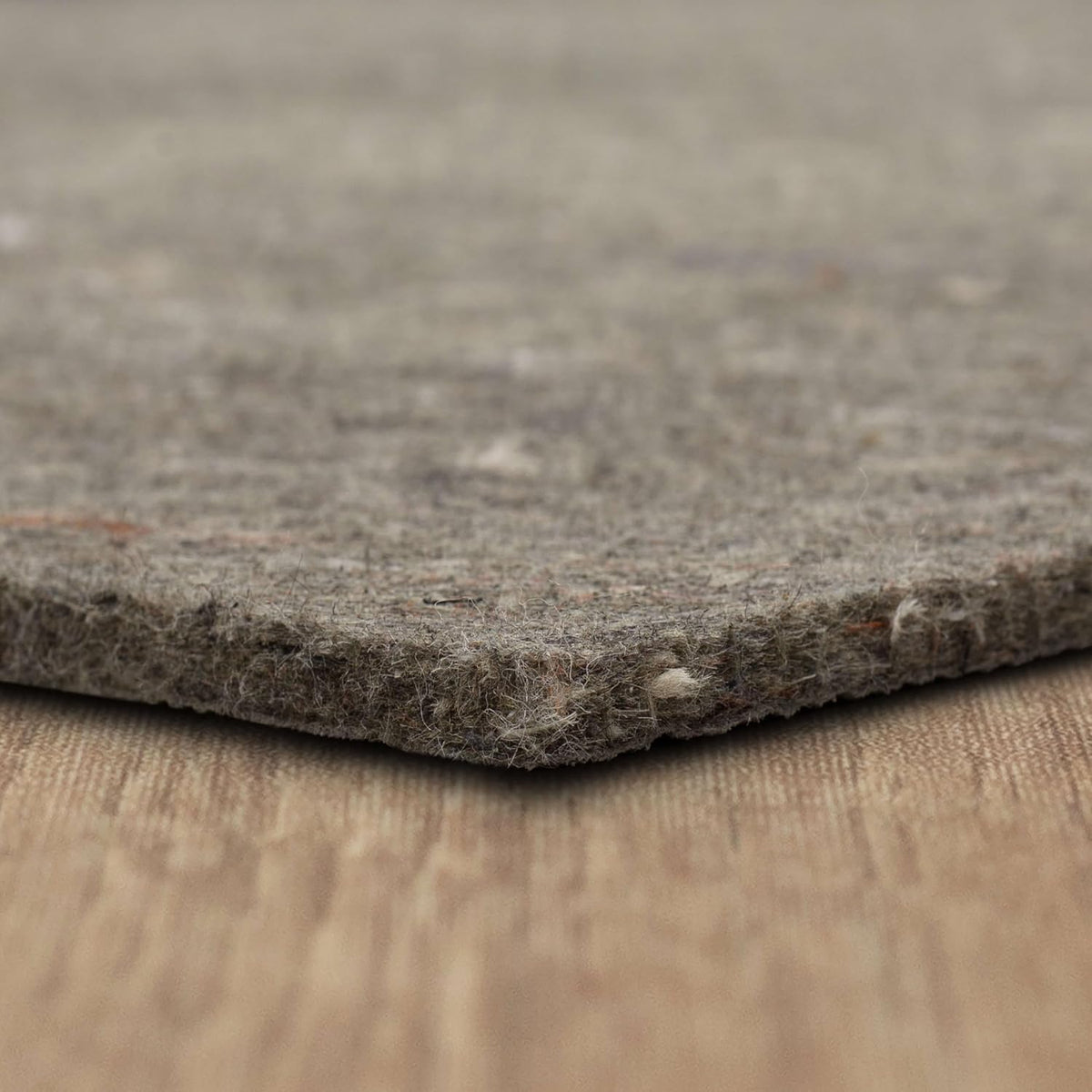 Angled macro of recycled-fiber pad edge highlighting loose fibers and small colored flecks in the material.