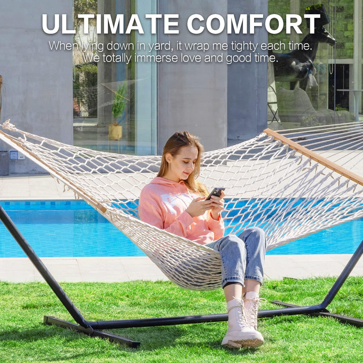 Natural rope hammock with hardwood spreader bar and pillow on a steel stand, poolside view with seated model