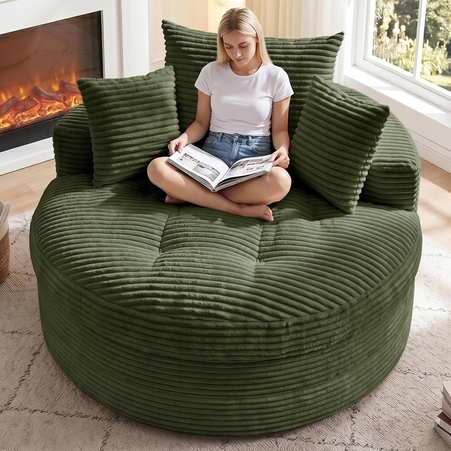 Top-front view of the same round corduroy chaise in olive green with three matching pillows and a person reading.