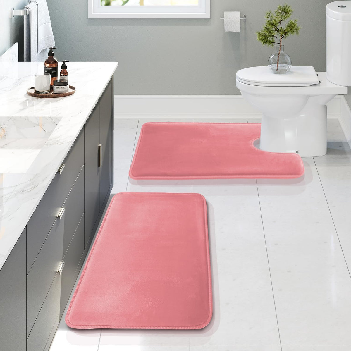 Bathroom scene with two pink memory-foam rugs placed on a tiled floor near a vanity and toilet