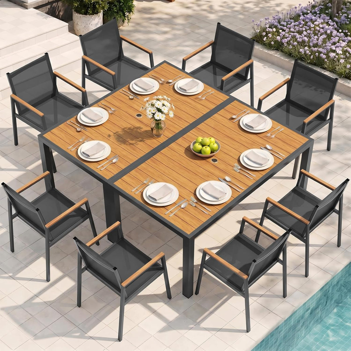 A light-wood outdoor dining table set with eight charcoal mesh chairs around a tiled poolside patio.