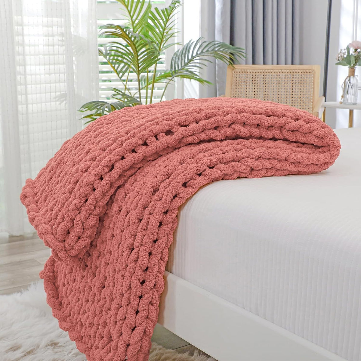 Folded chunky coral knit throw layered over the edge of a white bed in a bright bedroom.