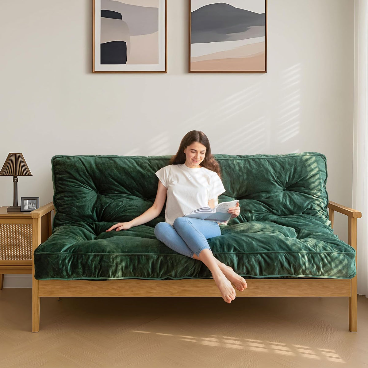 Person sitting on a dark green tufted futon mattress placed on a wooden sofa frame, front view