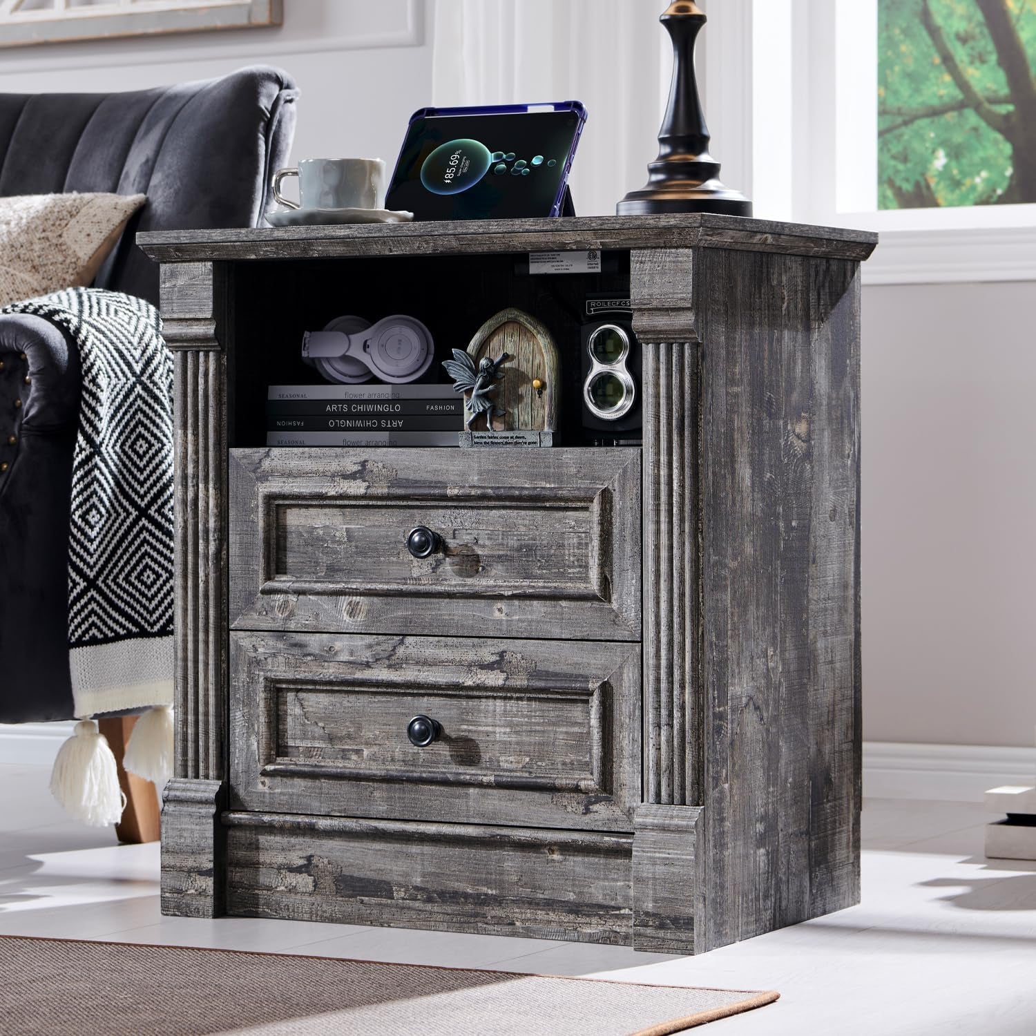 Angled view of a small gray wood nightstand with open cubby and two drawers, decor on top.