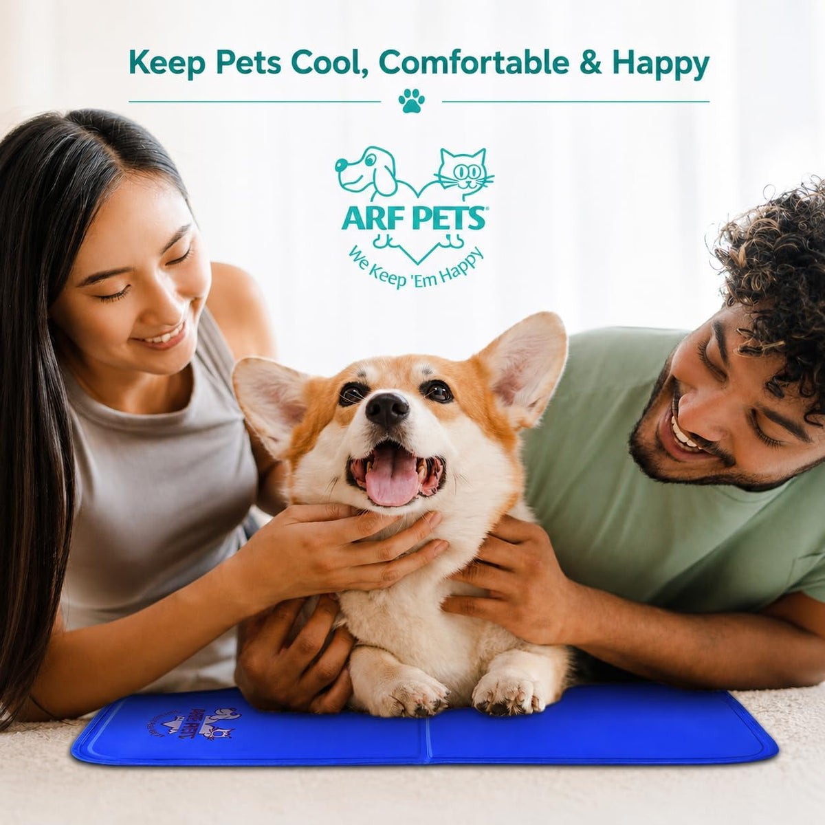 Smiling couple petting a happy corgi that sits on a blue cooling mat on a light carpet.