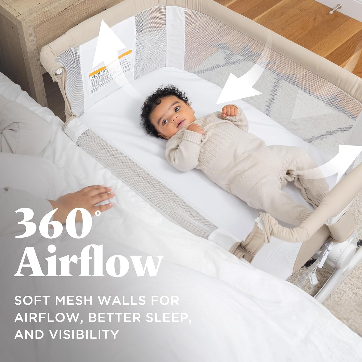 Top view of a baby lying in a beige mesh-sided bassinet positioned next to an adult bed.