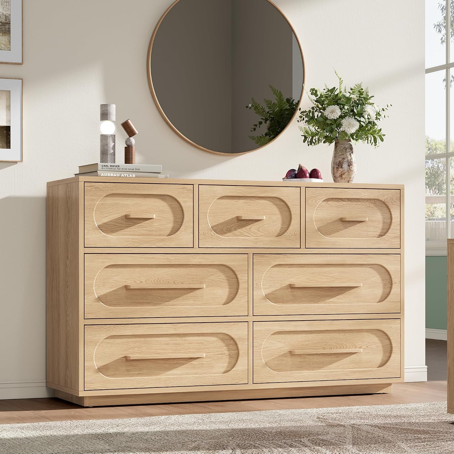 Light oak 8-drawer dresser with oval recessed drawer fronts and minimal handles under a round wall mirror