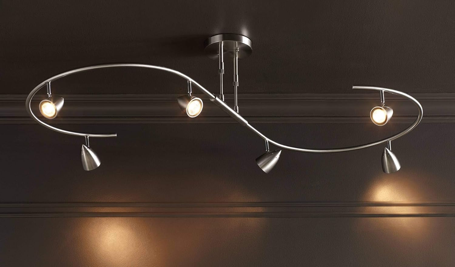 Fixture installed on a dark ceiling, six lights producing warm pools of light on a textured wall below.