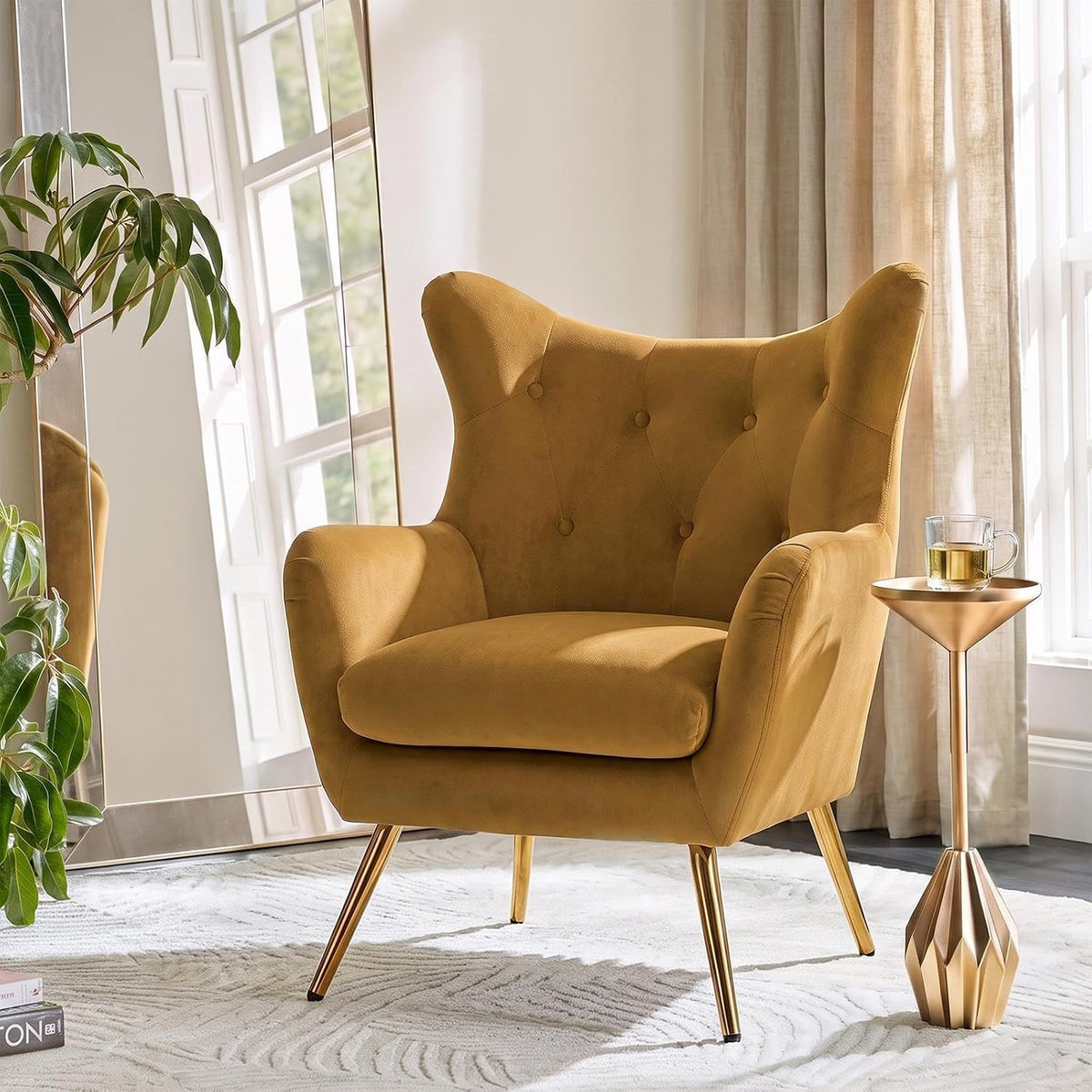 Mustard velvet wingback chair with button tufting and gold legs beside a metallic side table.