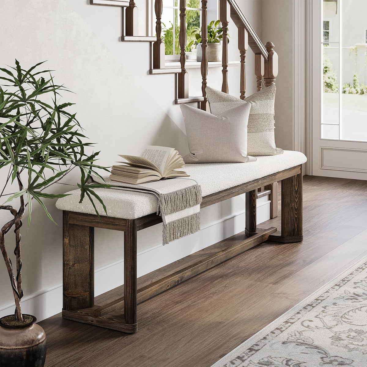 Entryway bench with white cushion and weathered wood frame beside a staircase, styled with pillows and a book